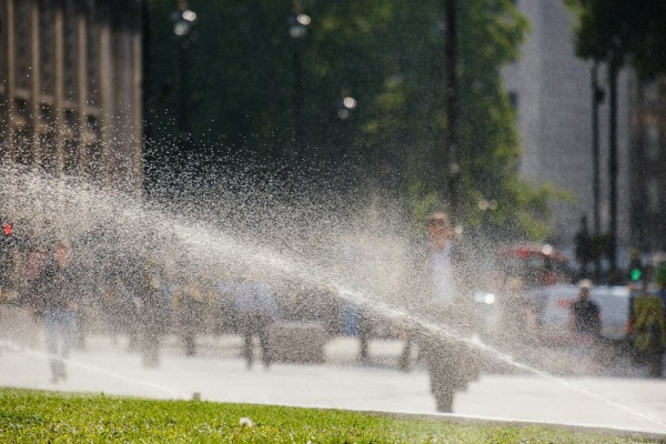 Sprinkler watering lawn in downtown area with man walking in the background